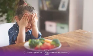 عکس دختر بچه ای که چشم های خود را بسته و جلوی او روی میز بشقاب سبزیجات قرار دارد - رژیم لاغری