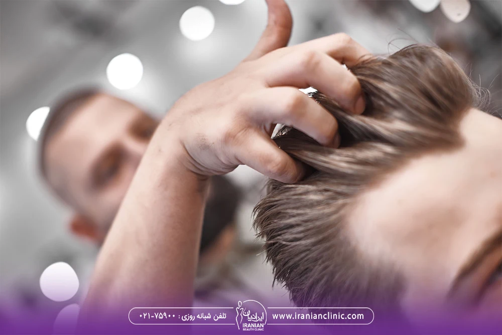 آرایشگر که انگشتانش را داخل موهای پرپشت مرد جوان برده است - مراقبت های بعد از کاشت مو