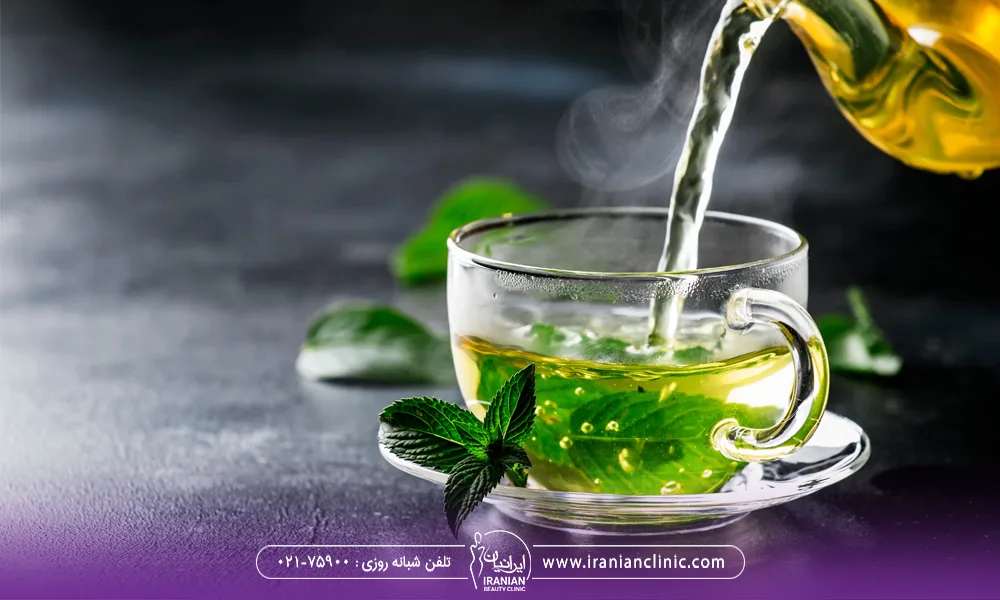 عکس یک برگ چای سبز داخل لیوان شیشه ای که از داخل قوری روی آن چای سبز ریخته می شود - چای سبز برای لاغری