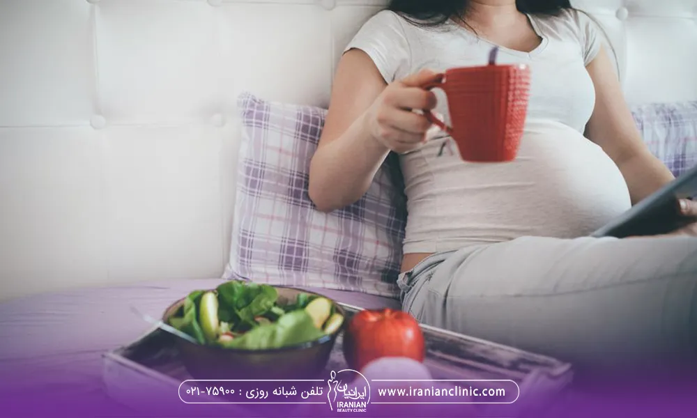 یک خانم باردار که در حال خوردن میان وعده است و یک لیوان در دست دارد