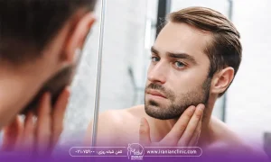 مردی که در آینه در حال نگاه کردن و بررسی کم پشتی ریش های صورتش است- عوارض کاشت ریش و سبیل