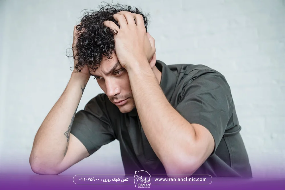 مرد جوان که دست خود را داخل موهای فر خود فرو برده است و ناراحت است