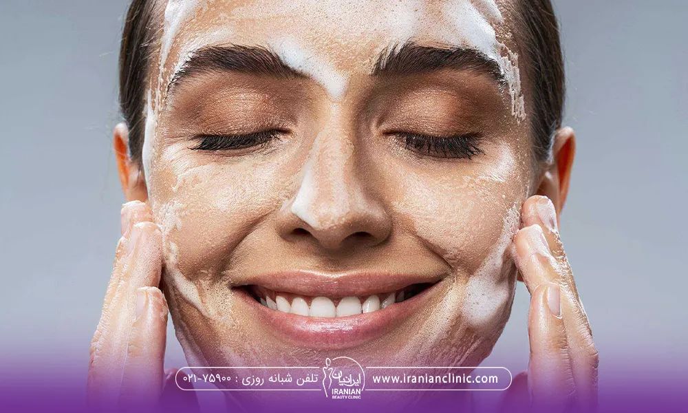 زن جوانی که لبخند زده و در حال شستن صورت خود است
