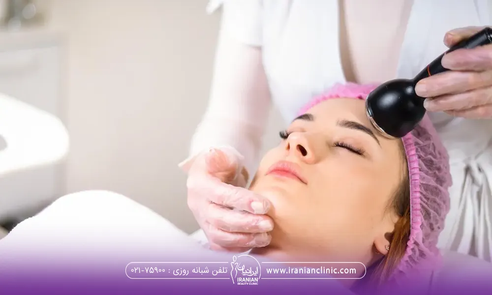فردی که روی تخت خوابیده است و کلاه مخصوص صورتی به سر دارد و اپراتوری که بالاسر وی با دستگاهی که در دست دارد مشغول درمان پوست پیشانی او است و با انگشتان دست دیگر زیر چانه فرد را گرفته است