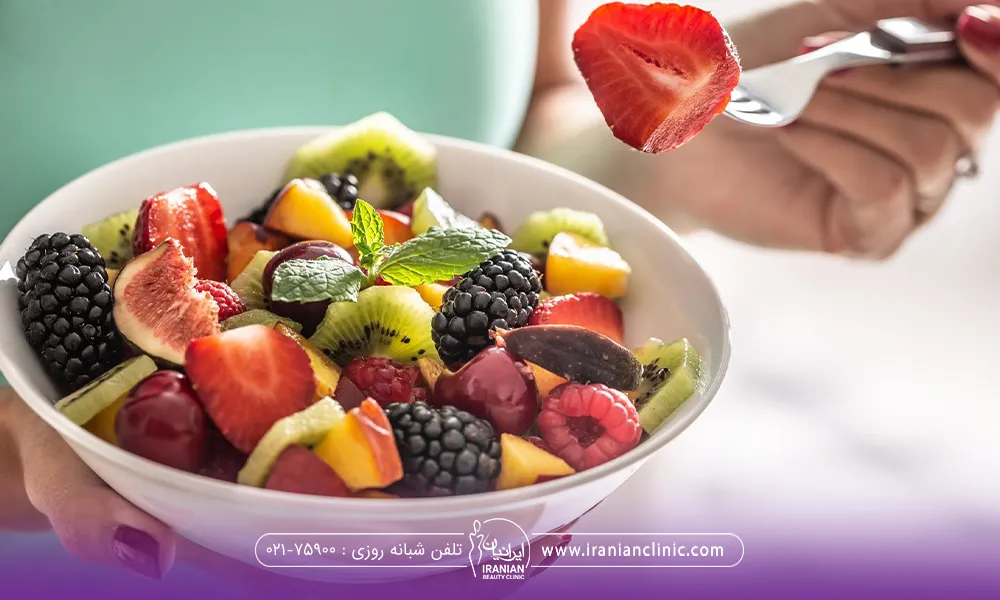 فردی که ظرف میوه دستش است و با چنگال در حال خوردن میوه است