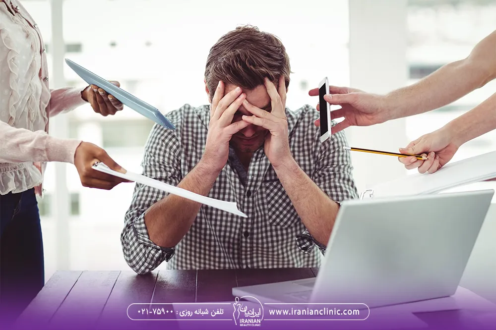 مردی که دچار استرس است و افراد زیادی در محیط کار در اطراف او هستند
