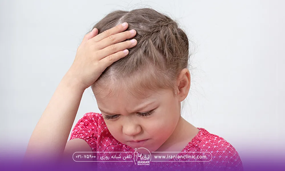 کودکی که سرش پایین است و یک دست خود را روی سرش گذاشته و از ریزش موی خود ناراحت است