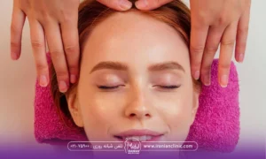 خانم خوشحالی که خوابیده است و چشم هایش بسته است و دستان فردی که از بالای سر او در حال انجام ماساژ شقیقه او است - ماساژ صورت برای جوانسازی