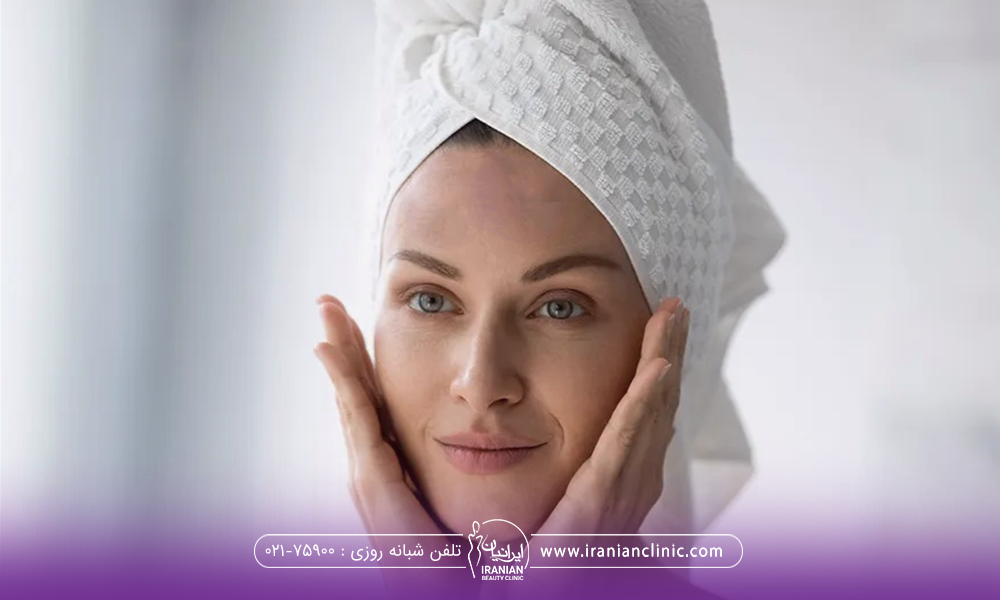 خانمی که دور سرش حوله پیچیده و دو دست خود را به صورتش چسبانده است